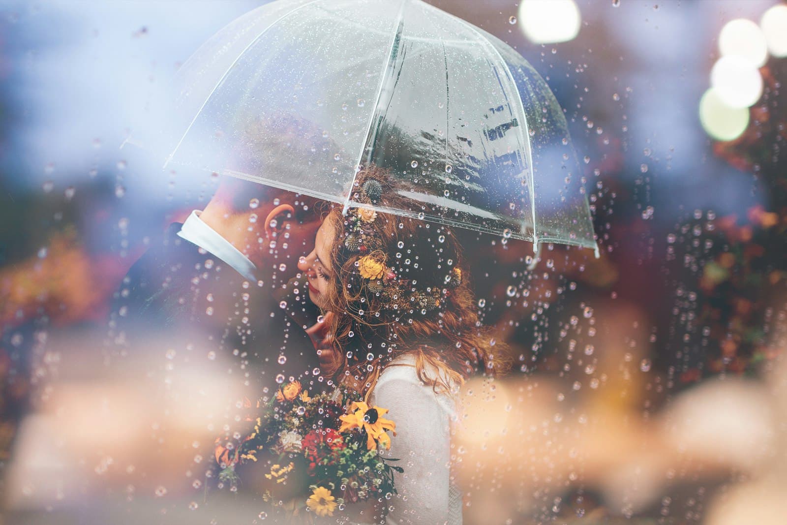 Les mariés s’embrassent sous un parapluie transparent constellé de gouttes de pluie
