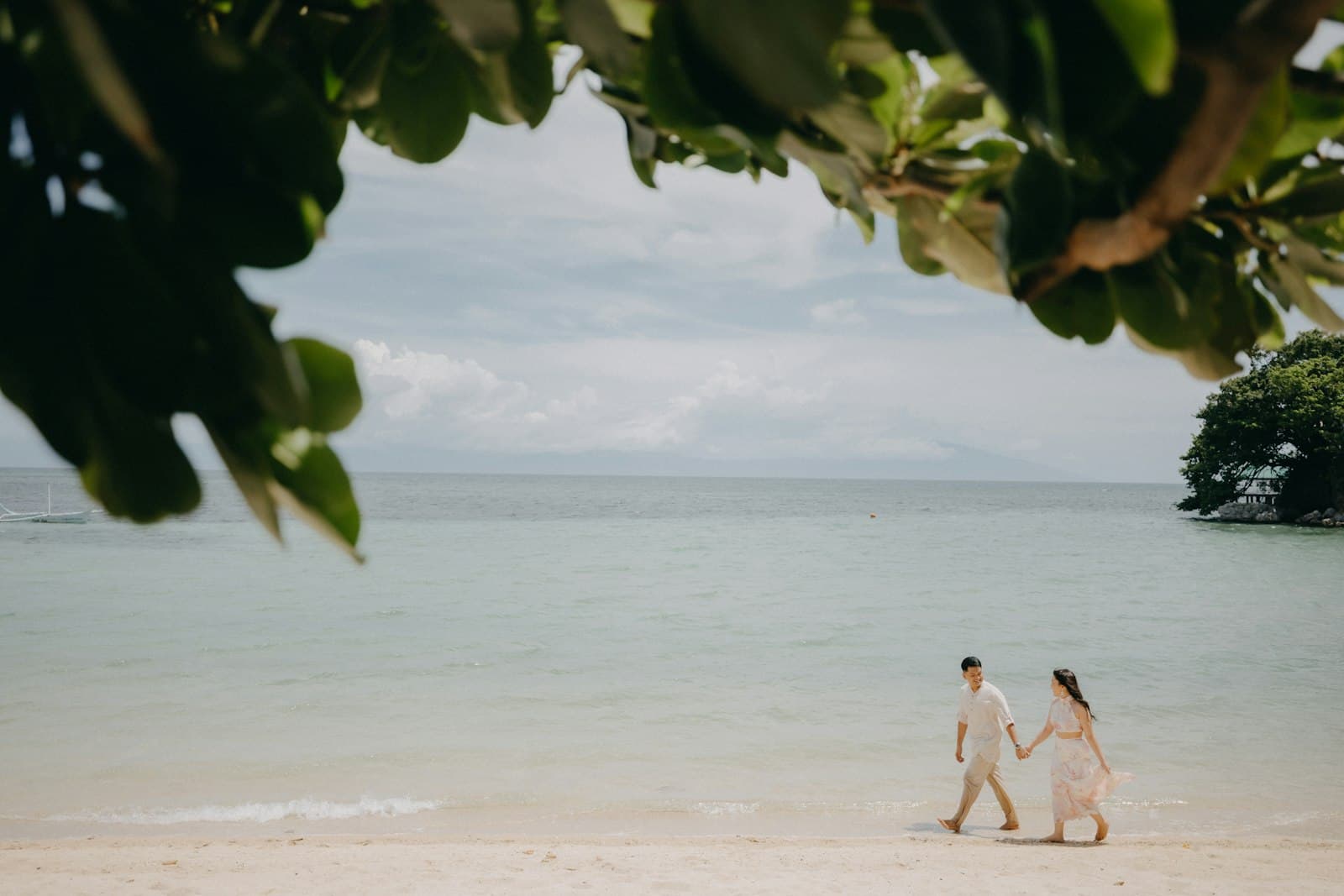 Jeunes mariés se tenant la main sur une plage tropicale, vus à travers le feuillage