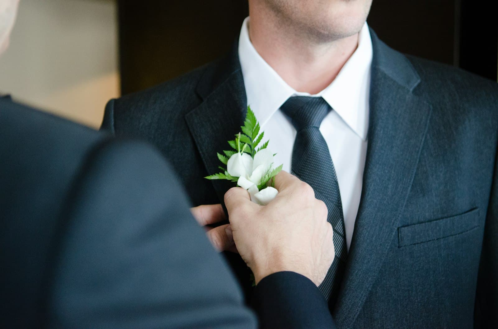 Un témoin épingle une boutonnière fleurie au revers du costume sombre du marié