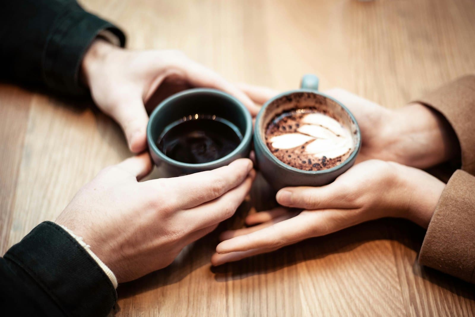 Deux mains qui rapprochent leurs tasses de café sur une table en bois