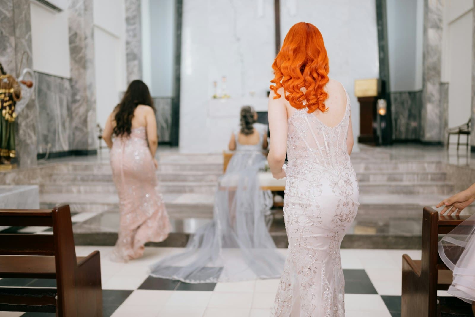Invitées en robes de cérémonie claires remontant l’allée d’une salle de mariage