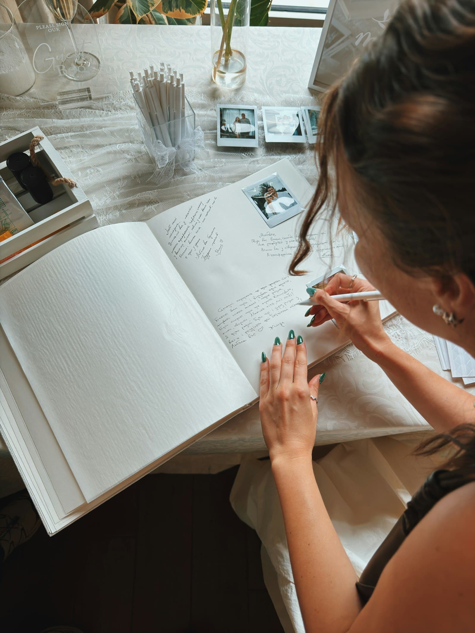 Une invitée écrit un message dans un livre d’or de mariage ouvert, entouré de photos instantanées