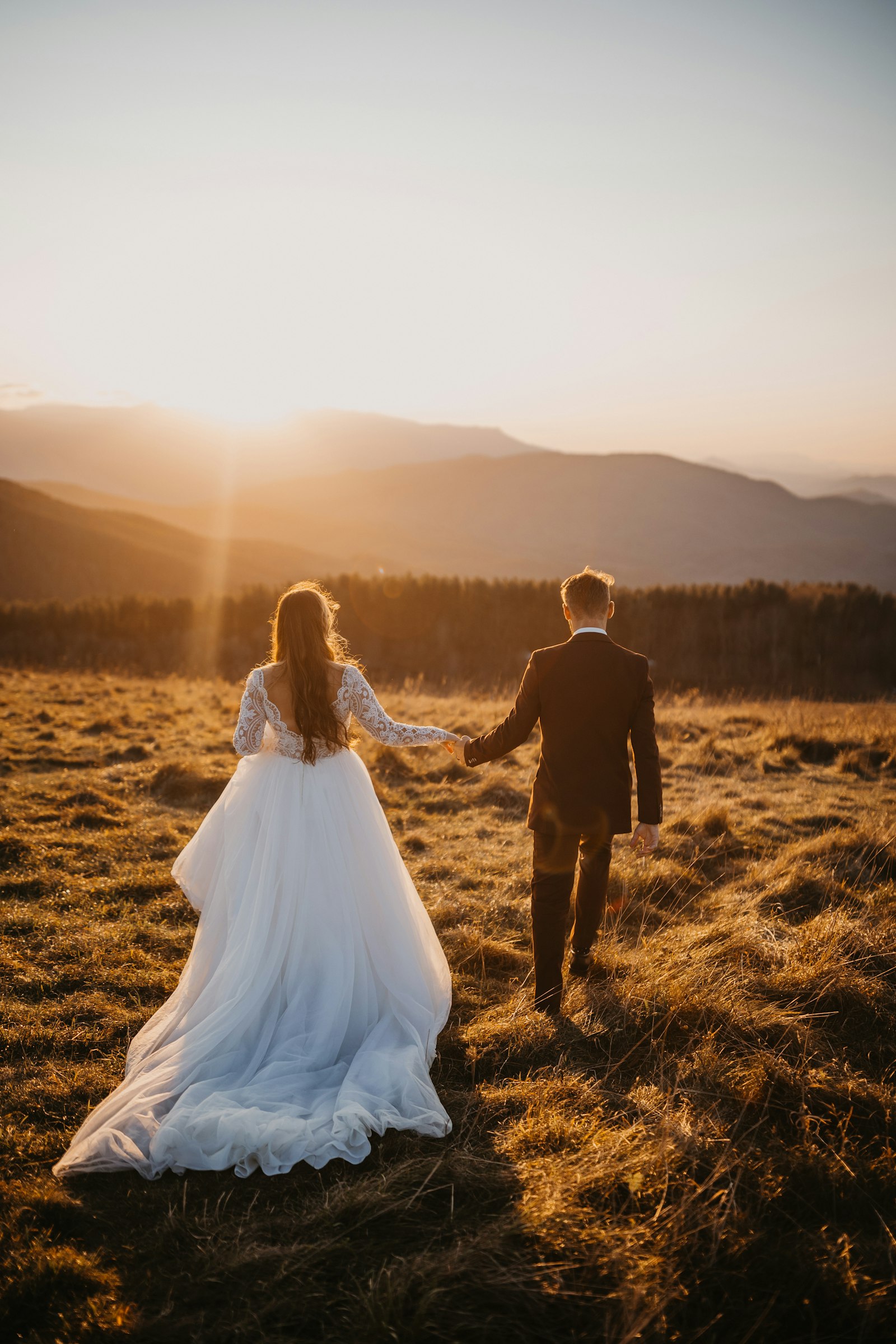 Couple de mariés marchant main dans la main au coucher du soleil
